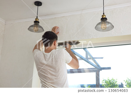 Caucasian plasterer man with a spatula applying finishing putty on a window opening Caucasian plasterer man with a spatula applying finishing putty on a window opening 130654083
