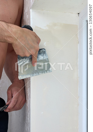 Caucasian plasterer man with a spatula applying finishing putty on a window opening Caucasian plasterer man with a spatula applying finishing putty on a window opening 130654097