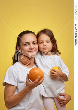Cheerful little child girl with mother holding lemon and grapefruit on yellow background. happy family having fun together 130654109