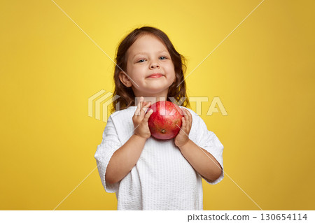 cute little child girl holding a pomegranate on yellow background. 130654114
