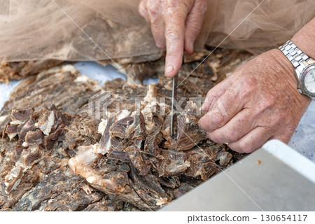 Hands of farmer cutting dried Tsamarella meat slices with a knife. Cyprus 130654117