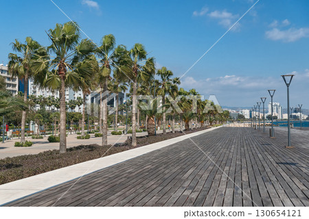Empty wooden promenade running along coastline with palm trees. Limassol, Cyprus 130654121