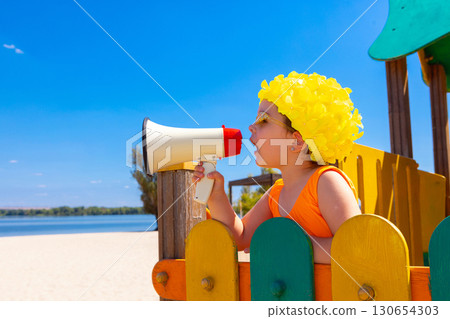Child in yellow swim cap shouting into megaphone at beach with energetic face Child in yellow swim cap shouting into megaphone at beach with energetic face 130654303