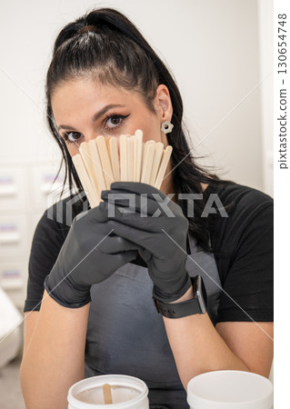 Beautician woman in black gloves holding wooden spatulas for waxing and sugaring procedure 130654748