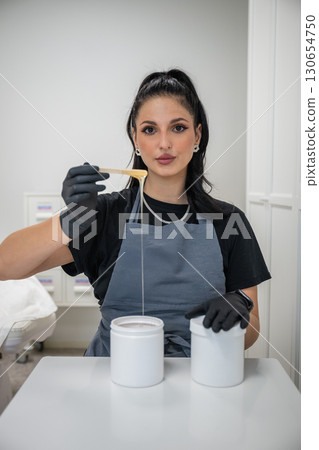 Beautician woman in black gloves holding jar of sugaring paste for hair removal procedure Beautician woman in black gloves holding jar of sugaring paste for hair removal procedure 130654750