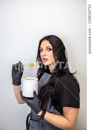 Beautician woman in black gloves holding jar of sugaring paste for hair removal procedure Beautician woman in black gloves holding jar of sugaring paste for hair removal procedure 130654752