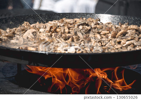 Chef cooking mushrooms over an open fire in a large pan Chef cooking mushrooms over an open fire in a large pan 130655026