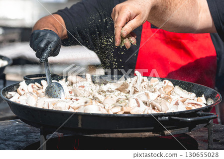 Chef seasoning sliced mushrooms in a large pan over an open fire 130655028