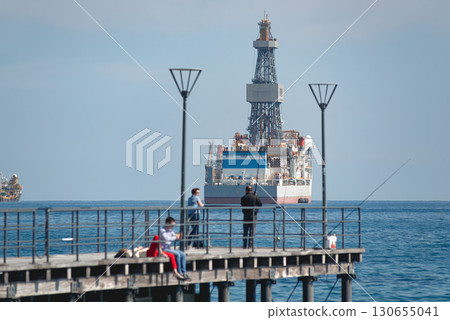 People fishing on pier with Drilling vessel in background in Akrotiri Bay, limassol 130655041