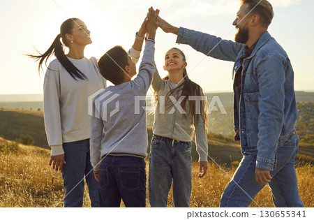 Happy family standing in the field with two kids and putting their hands in stack. 130655341