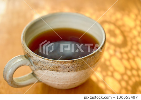 Close-up of a mug of coffee and the silhouette of lace curtains. 130655497