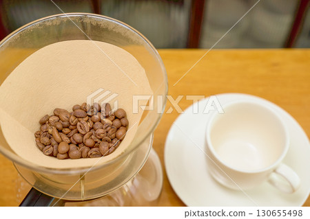 一個滴濾壺,裝有兩杯輕度烘焙的咖啡豆和一杯白咖啡。 一個滴濾壺,裝有兩杯輕度烘焙的咖啡豆和一杯白咖啡。 130655498