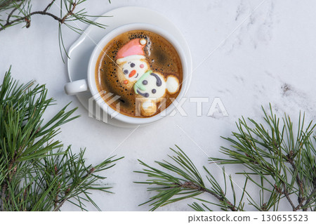 Cup of coffee with marshmallows. Marshmallow snowman in a Santa Claus hat. Winter drink in the snow. Christmas tree. Top view Cup of coffee with marshmallows. Marshmallow snowman in a Santa Claus hat. Winter drink in the snow. Christmas tree. Top view 130655523
