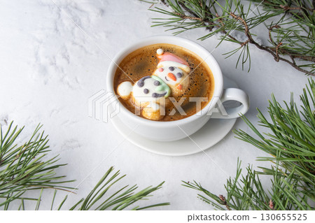 Cup of coffee with marshmallows. Marshmallow snowman in a Santa Claus hat. Winter drink in the snow. Christmas tree. Top view Cup of coffee with marshmallows. Marshmallow snowman in a Santa Claus hat. Winter drink in the snow. Christmas tree. Top view 130655525