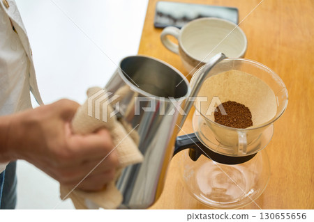 A man pours the first steaming water. A series of photos showing the process of brewing coffee using a paper drip. A man pours the first steaming water. A series of photos showing the process of brewing coffee using a paper drip. 130655656