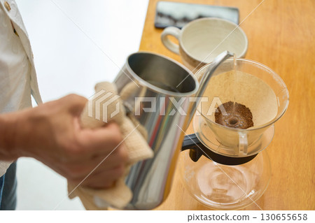 A man pours the first steaming water. A series of photos showing the process of brewing coffee using a paper drip. A man pours the first steaming water. A series of photos showing the process of brewing coffee using a paper drip. 130655658