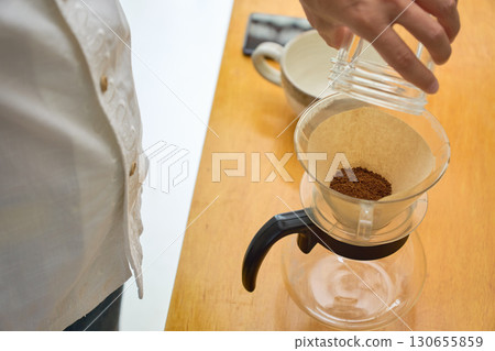 一位男士將磨好的咖啡豆倒入滴濾壺。一系列照片展示了滴濾咖啡的沖泡過程。 一位男士將磨好的咖啡豆倒入滴濾壺。一系列照片展示了滴濾咖啡的沖泡過程。 130655859