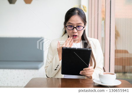 Asian businesswoman sitting in cafe using digital tablet computer looking shocked and surprised Asian businesswoman sitting in cafe using digital tablet computer looking shocked and surprised 130655941