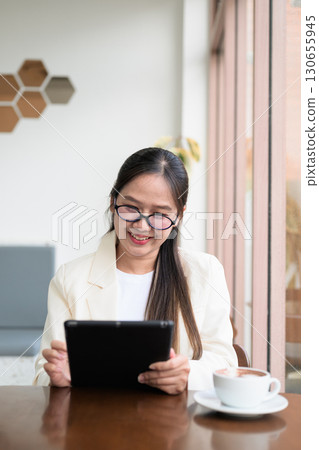 Asian businesswoman sitting in coffee shop restaurant using digital tablet computer smiling 130655945