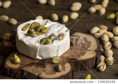 pistachios nuts are green in color along with whole cheese in white mold, delicious white soft cheese in mold and a large number of salted pistachios with and without cracked shells 130656299