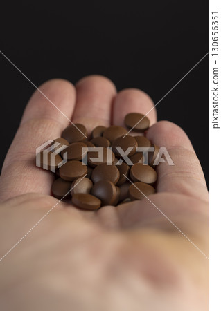 a large number of brown tablets without packaging are poured into your hand. a handful of brown pills in the man's hand 130656351
