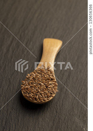 flax seeds poured into a wooden spoon on slate, glossy black surface with a wooden spoon filled with flax seeds 130656366