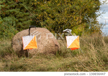Two orange and white orienteering prisms placed on a large mossy rock 130656447