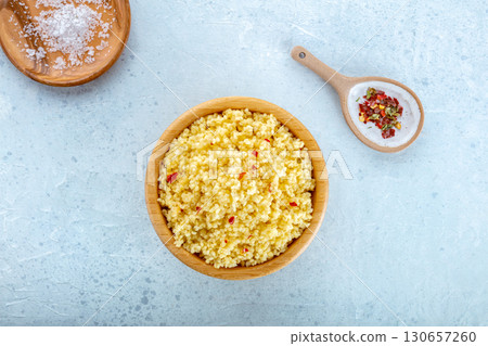 Cooked millet in a wooden bowl on a blue background, with salt and pepper 130657260