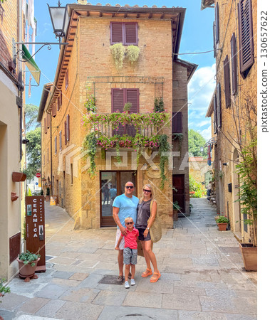 Tourists enjoying summer holidays in Siena old town. Smiling parents and kid standing in front of rustic Italian architecture with balcony flowers 130657622