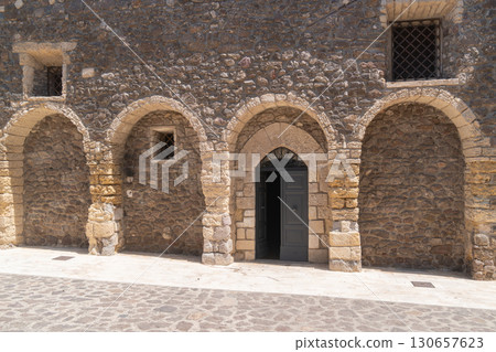 An ancient stone wall features multiple arches and a partially open wooden door, revealing a glimpse inside. The medieval architecture reflects a rich historical heritage An ancient stone wall features multiple arches and a partially open wooden door, revealing a glimpse inside. The medieval architecture reflects a rich historical heritage 130657623