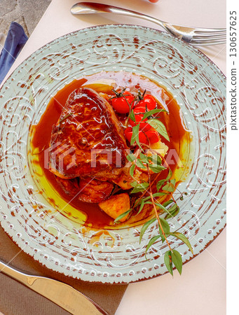 Gourmet steak dish served with roasted potatoes and cherry tomatoes garnished with fresh herbs. A rich sauce enhances the exquisite presentation on a decorative plate. Gourmet steak dish served with roasted potatoes and cherry tomatoes garnished with fresh herbs. A rich sauce enhances the exquisite presentation on a decorative plate. 130657625