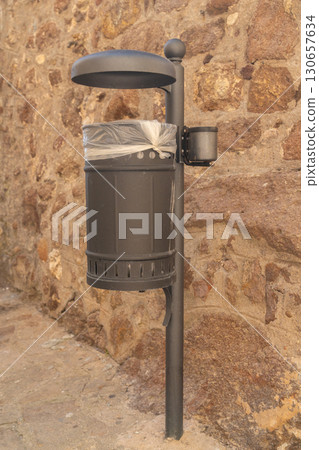 Urban trash can equipped with a plastic liner against a textured stone wall. The sturdy design and practical placement make it ideal for maintaining cleanliness in busy public spaces. 130657634