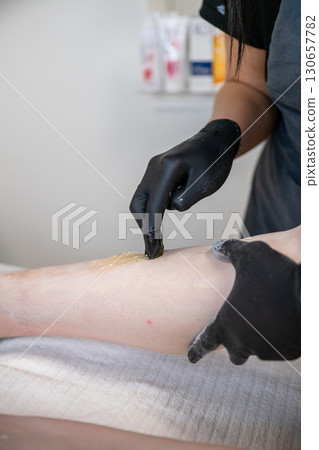 Beautician applying sugaring paste on female leg during professional hair removal procedure 130657782