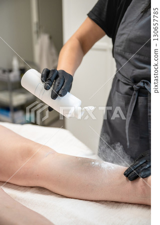 Beautician applying talcum powder on female leg before professional hair removal procedure Beautician applying talcum powder on female leg before professional hair removal procedure 130657785