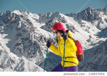 Blurred Woman Ascends Snow-Covered Slope Under Bright Winter Sunlight in Mountainous Terrain 130657950