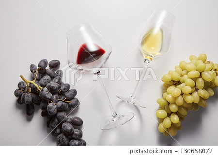 Wineglasses with white, red beverages are between grapes. 130658072
