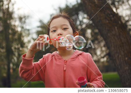 Girl Blowing Bubbles in Park 130658075