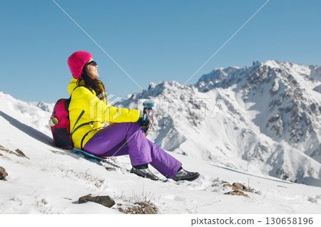 Woman Sitting on Snow Covered Slope in Sunny Day 130658196