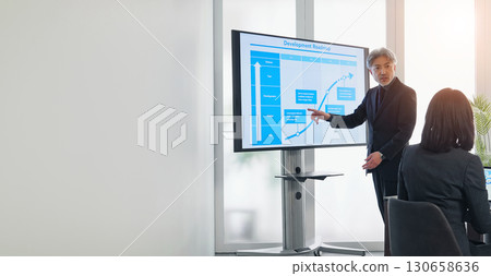 A middle-aged male business person giving an explanation in front of a large screen monitor A middle-aged male business person giving an explanation in front of a large screen monitor 130658636