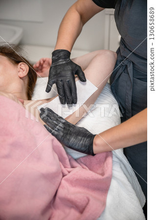 Beautician applying wax strip on female armpit during professional hair removal procedure 130658689