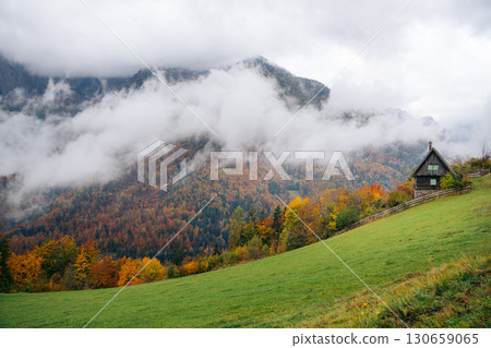 Autumn colors surround a cabin in Slovenia, with mountains shrouded in mist 130659065