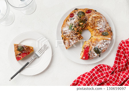 A round cake on a white plate with a slice served, surrounded by wine glasses and a checkered cloth A round cake on a white plate with a slice served, surrounded by wine glasses and a checkered cloth 130659097