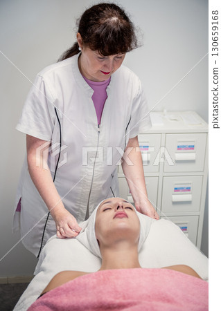 Beautician preparing female client for cosmetic facial treatment in professional beauty salon Beautician preparing female client for cosmetic facial treatment in professional beauty salon 130659168
