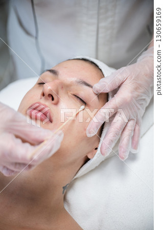 Beautician applying cosmetic treatment on female face with cotton swab in beauty salon Beautician applying cosmetic treatment on female face with cotton swab in beauty salon 130659169