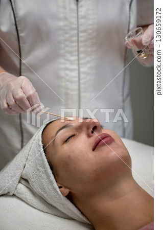 Beautician applying cosmetic treatment on female face with cotton swab in beauty salon Beautician applying cosmetic treatment on female face with cotton swab in beauty salon 130659172