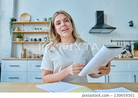 Webcam portrait female university student, sitting at home at the table with textbooks 130659301
