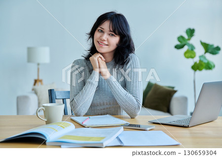 Portrait of young woman university student sitting at desk with laptop, looking at camera 130659304