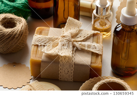 Handmade body care items, natural soap, wrapped in kraft paper and decorated with a crocheted ribbon. Around are placed bottles of oil and other details for decoration Handmade body care items, natural soap, wrapped in kraft paper and decorated with a crocheted ribbon. Around are placed bottles of oil and other details for decoration 130659345
