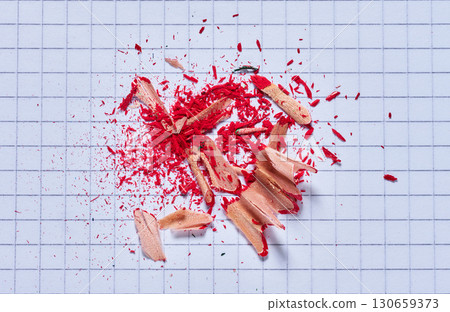 Close-up of red pencil shavings and filings lying on a piece of squared paper 130659373