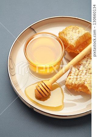 Bowl of sweet honey, dippers and combs on plate on dark blue background. Vertical photo Bowl of sweet honey, dippers and combs on plate on dark blue background. Vertical photo 130660134